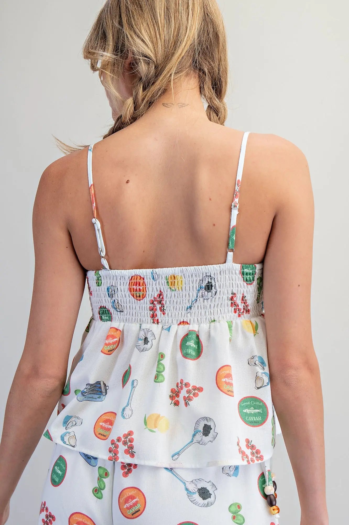 White Mediterranean-inspired food print babydoll top with adjustable beaded straps, gathered bust, and smocked back detail.