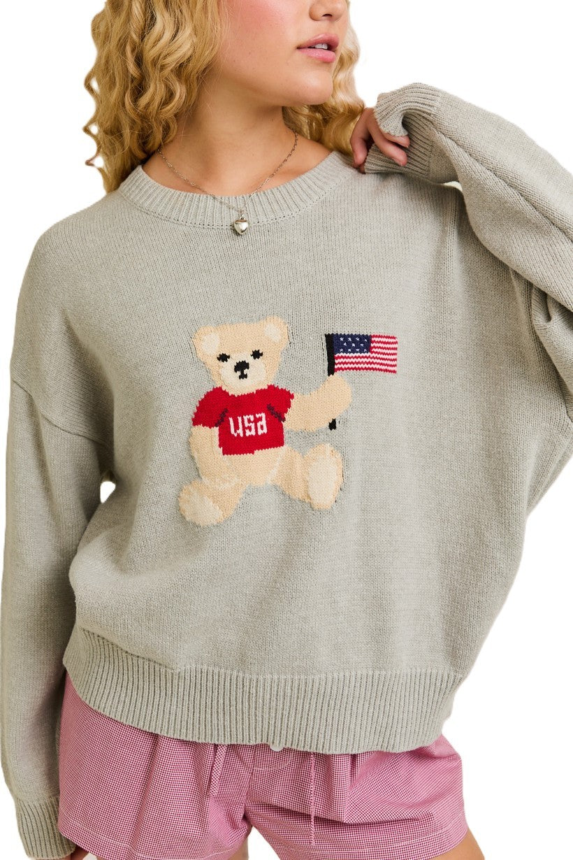 A cozy, cute, and patriotic sweater featuring an adorable teddy bear holding the USA flag—perfect for laid-back, stylish layering.