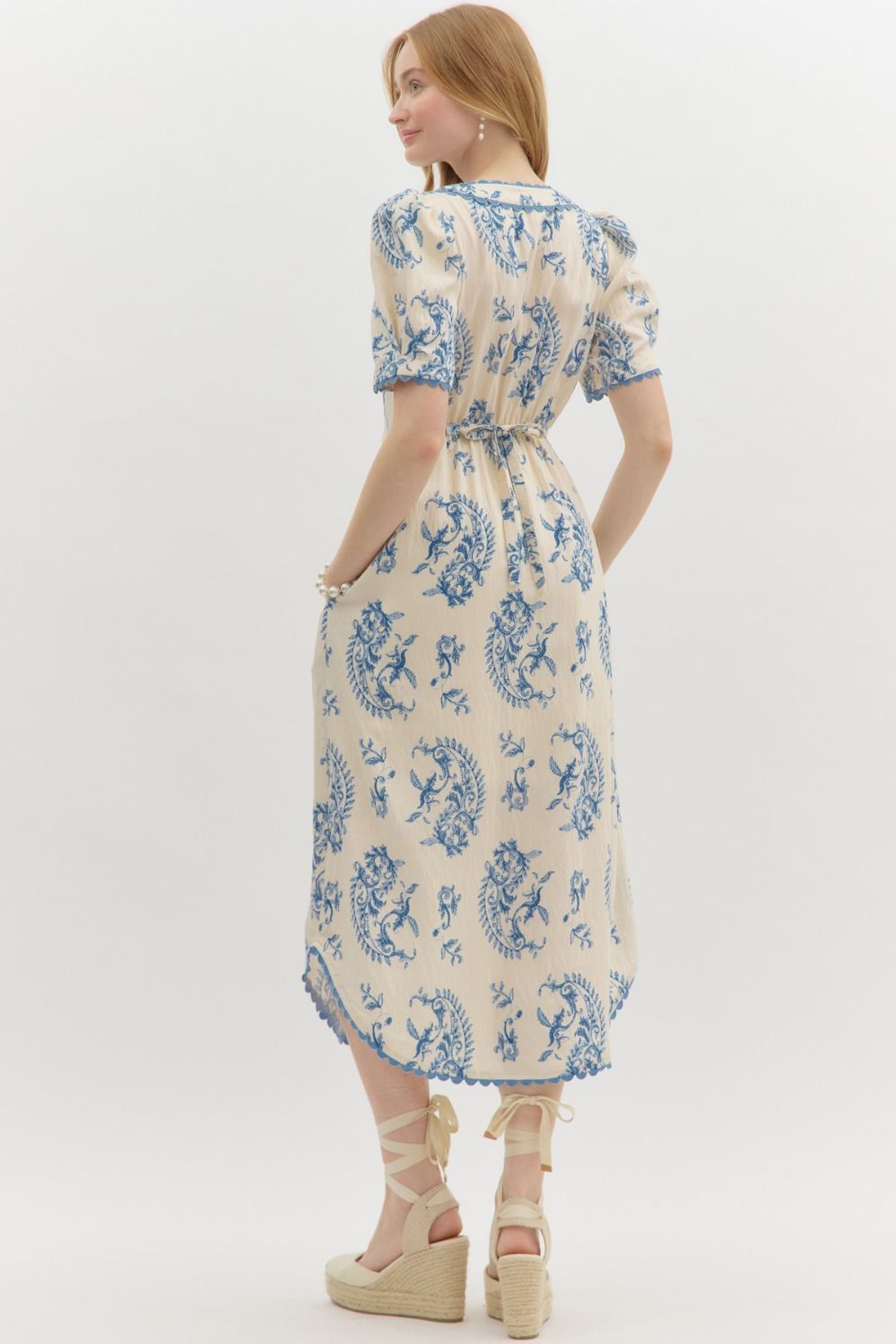 A pleated paisley midi dress with scalloped trim, self-tie waist, and graceful V-neckline.