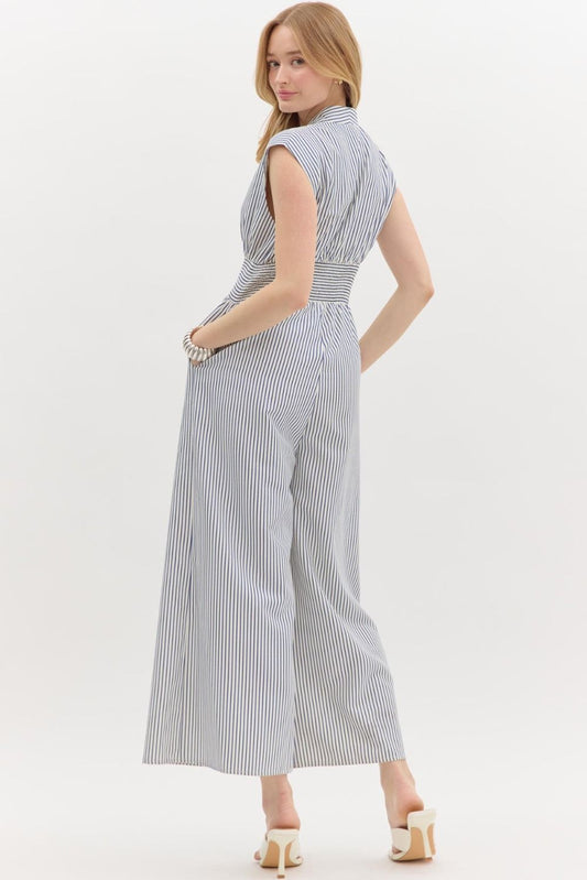 A sleek ankle-length jumpsuit with structured shoulders, front zipper, and smocked waist—tailored yet relaxed with coastal-cool appeal.