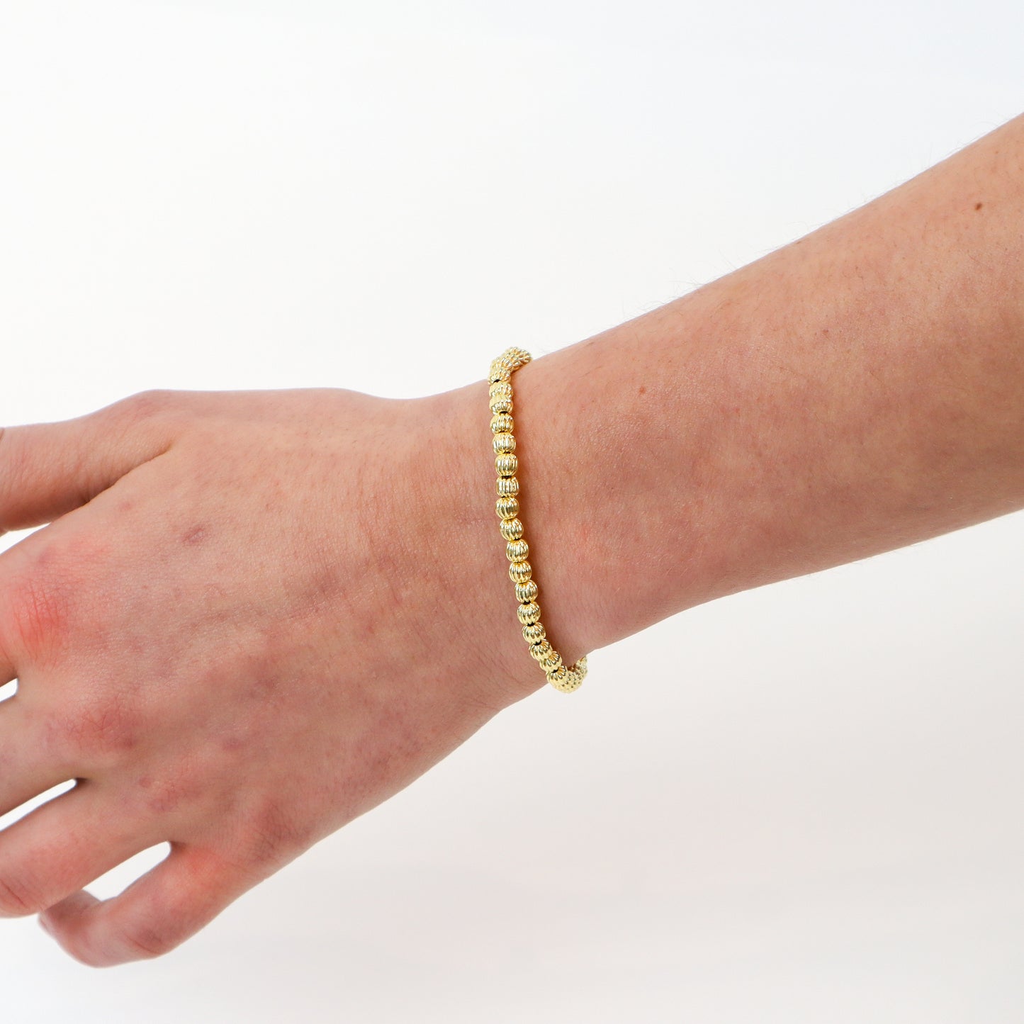 14k gold-filled textured beaded bracelet on wrist" | "Minimalist gold bracelet on white background