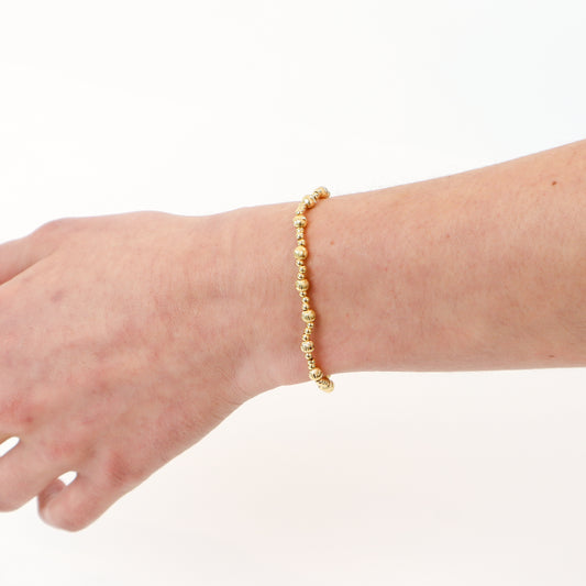 A delicate 14K gold-filled textured beaded bracelet displayed on a model's wrist, showcasing its elegant design and stackable style