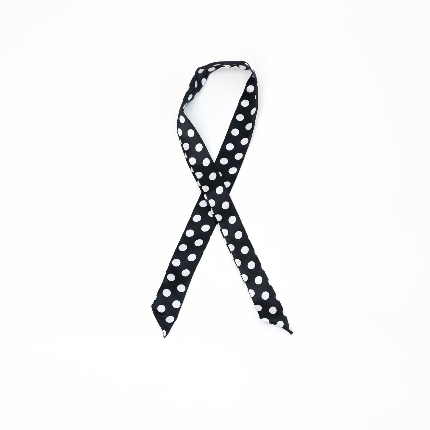 A slim twilly scarf with a classic black background and small white polka dots, tied in a loop.