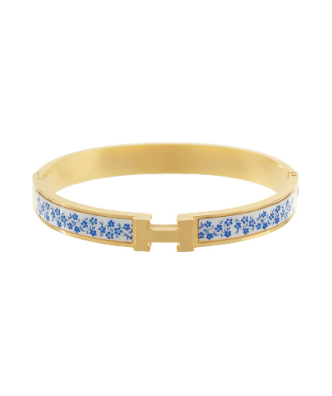 Blue Blossom Hinge Bangle featuring a gold-toned band with a white enamel inlay adorned with delicate blue floral blossoms.