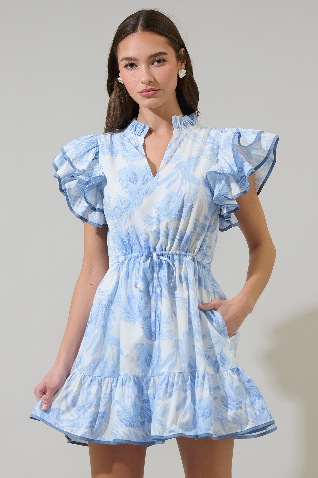 Blue and white palm-print mini dress with ruffled sleeves, a V-neckline, a cinched waist, and tiered hem, perfect for elegant summer outings.
