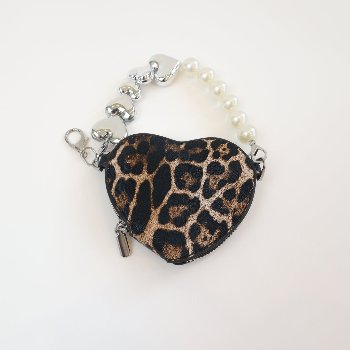 Trendy heart-shaped cheetah print purse with metallic heart charms and pearl wrist strap—perfect for carrying essentials in style.