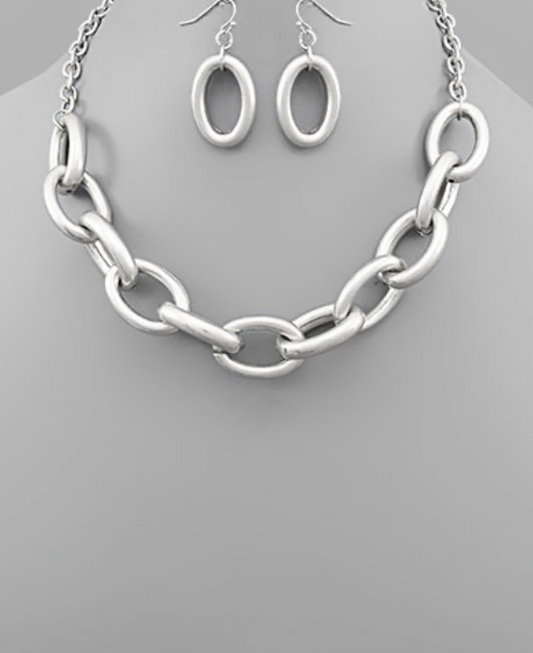 A chunky silver-toned chain link necklace with large, matte oval links, accompanied by matching oval hoop dangle earrings.