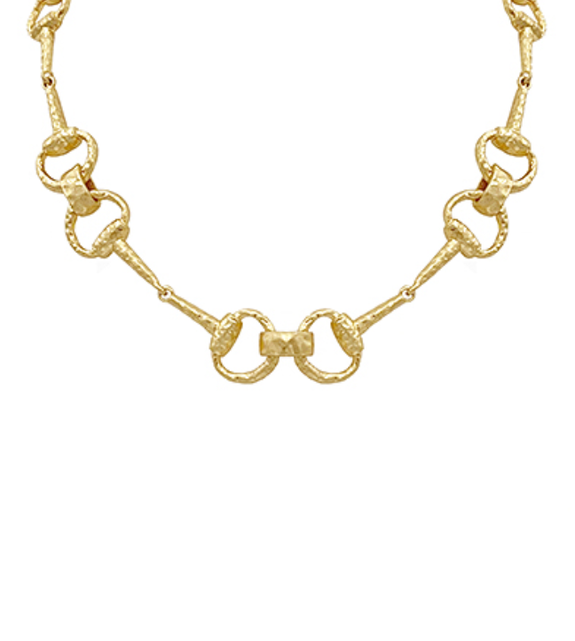 A striking gold-toned necklace featuring an open-link chain design, with each link shaped like a horsebit, creating a bold, interlocking pattern. The links have a textured or hammered finish.