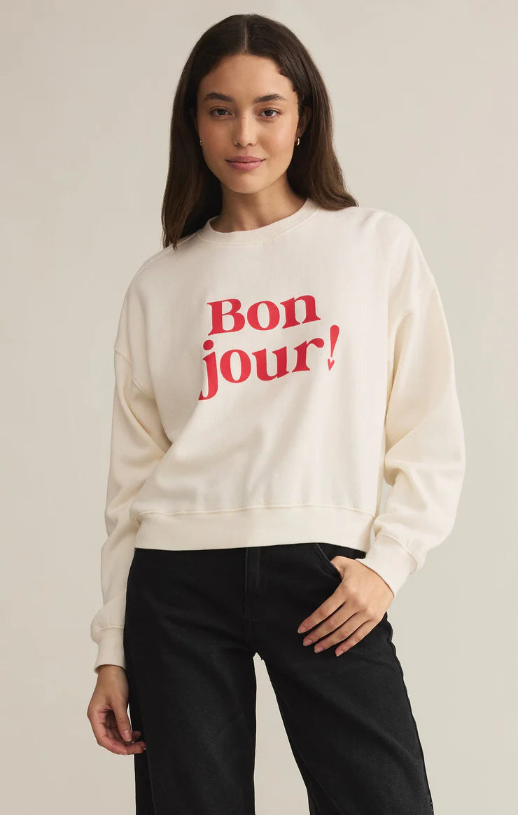 Soft fleece sweatshirt in sea salt color with bold red 'Bonjour!' graphic, featuring a relaxed fit and drop shoulder design for effortless comfort.