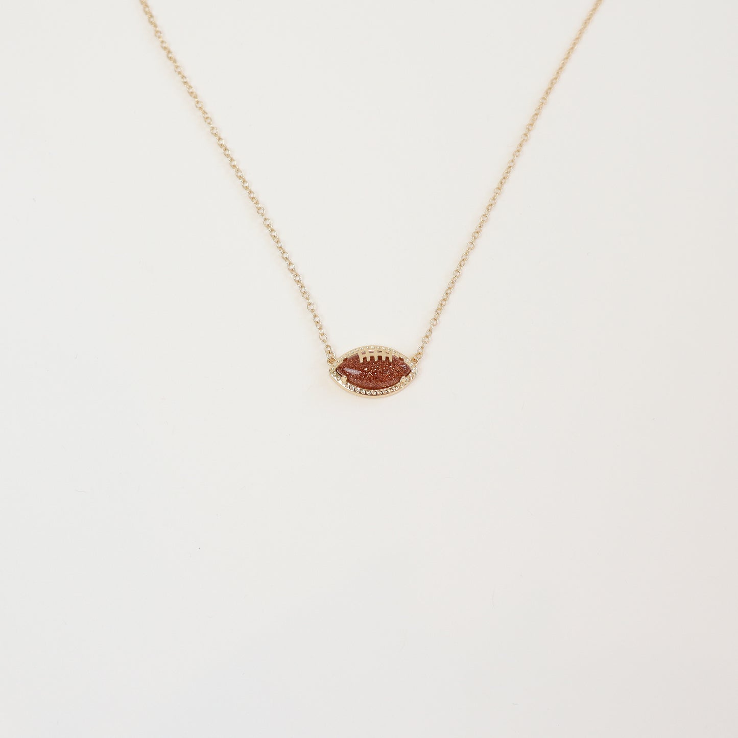 Gold football pendant necklace with sparkling rhinestone accents on a delicate gold chain, perfect for football fans and stylish game-day outfits