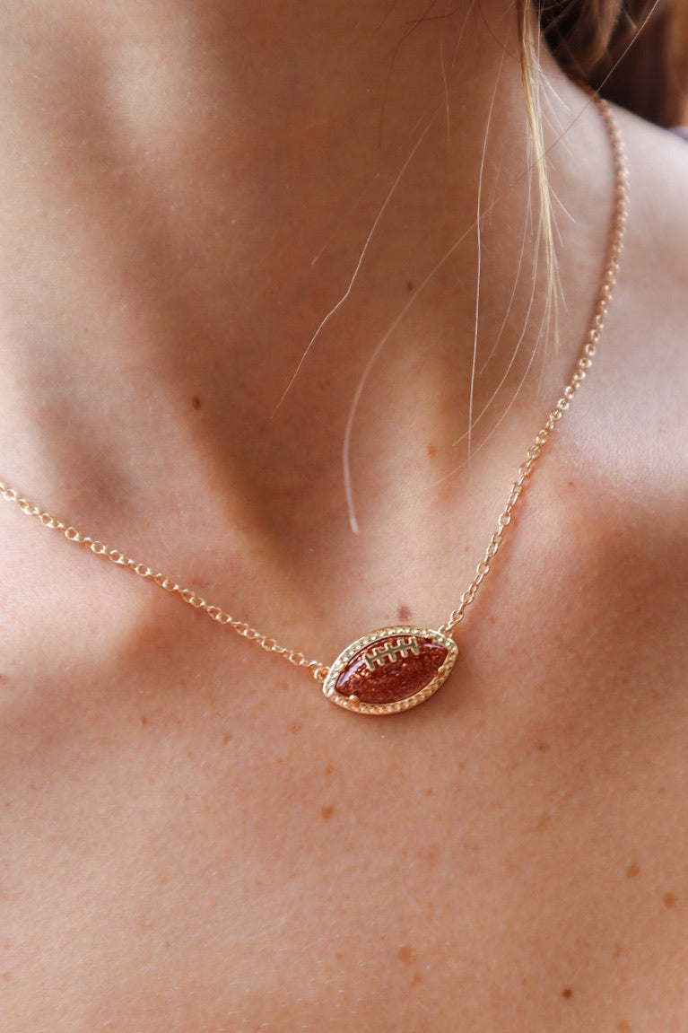 Gold football pendant necklace with sparkling rhinestone accents on a delicate gold chain, perfect for football fans and stylish game-day outfits