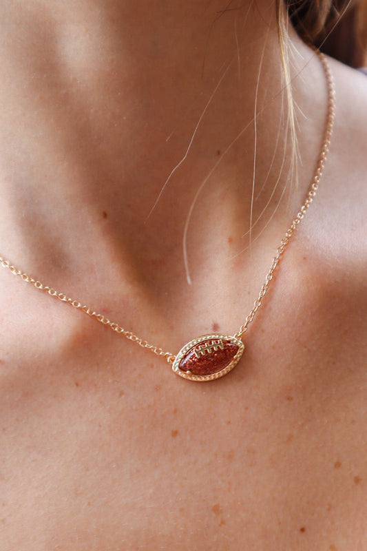 Gold football pendant necklace with sparkling rhinestone accents on a delicate gold chain, perfect for football fans and stylish game-day outfits