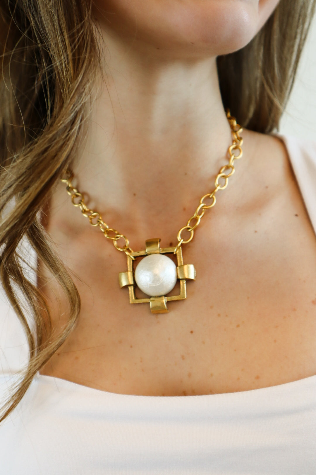 Gold-tone statement necklace featuring a large faux pearl pendant encased in a geometric frame, designed for a bold yet elegant look.