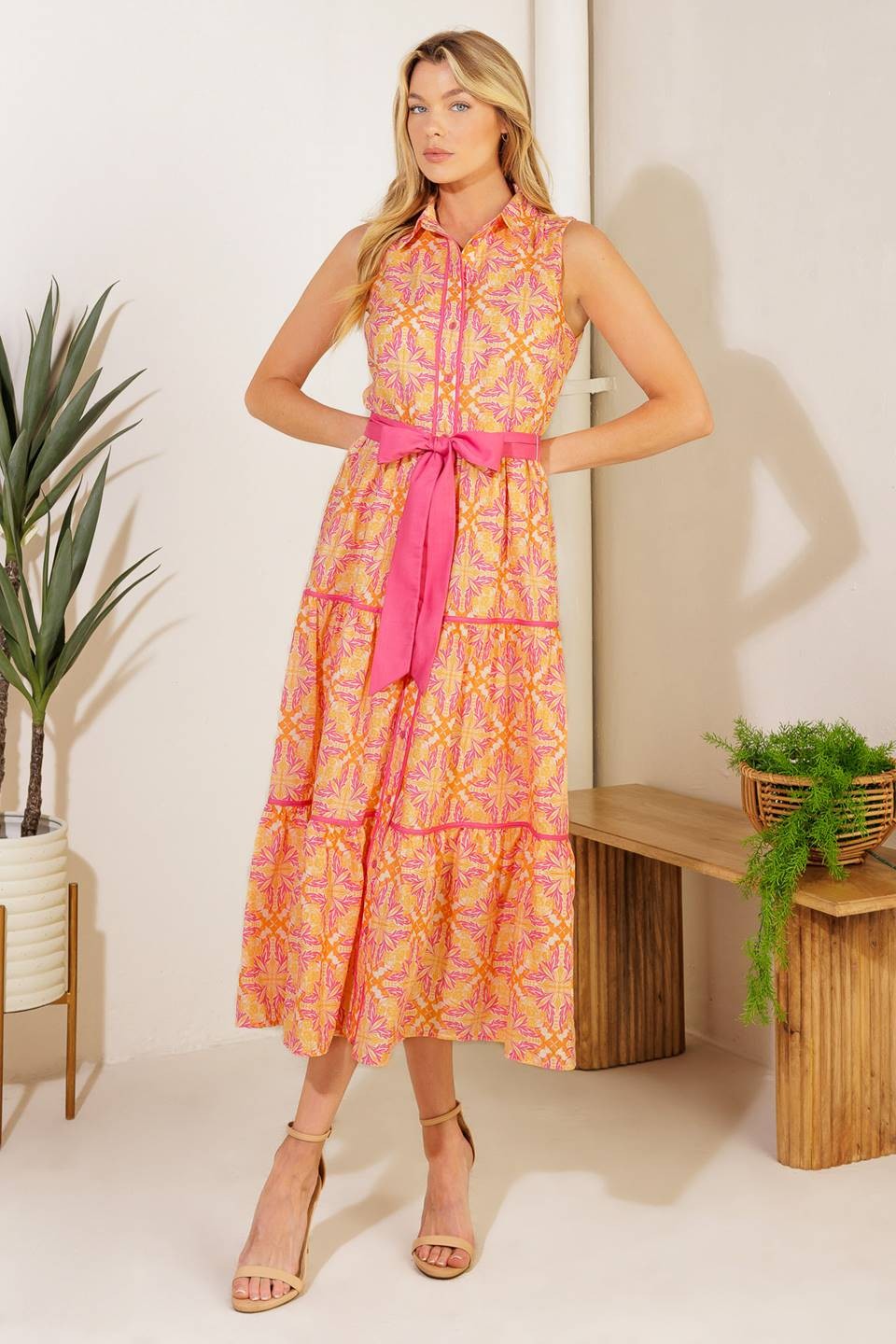 A sleeveless, button-down maxi dress featuring a vibrant pink, orange, and yellow floral-inspired print with a tiered skirt and a detachable pink waist belt for a flattering fit.