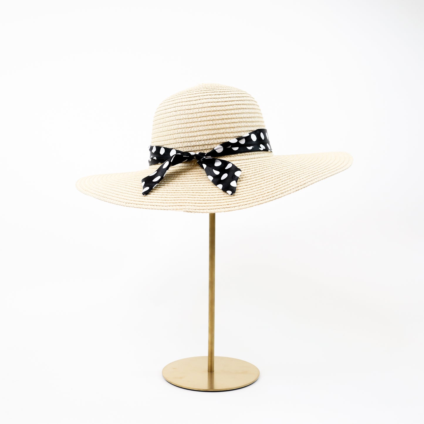 A timeless natural straw sun hat with a black and white polka dot ribbon bow, ideal for sun protection with a fashionable twist.