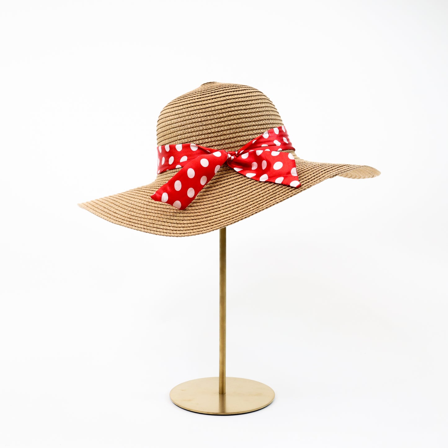 A classic natural straw sun hat accented with a bold red polka dot ribbon bow, adding a playful and vintage-inspired touch to your summer wardrobe.