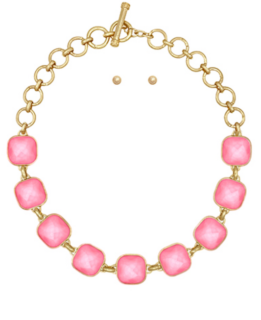 A gold-toned necklace featuring a series of evenly spaced, large, rounded square pink cabochon stones, linked by smaller gold rings, and fastened with a toggle clasp.