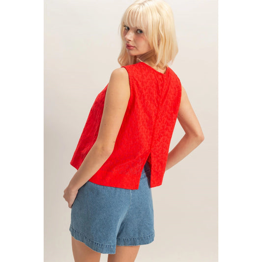 Woman wearing a red eyelet sleeveless tank top paired with high-waisted denim shorts, lightweight summer blouse with embroidered detailing.