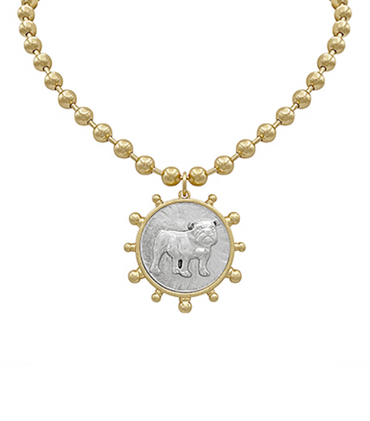 A gold-toned necklace with a beaded chain and a large circular medallion pendant featuring a silver-toned insert with a detailed bulldog illustration, encircled by gold-toned decorative nubs.