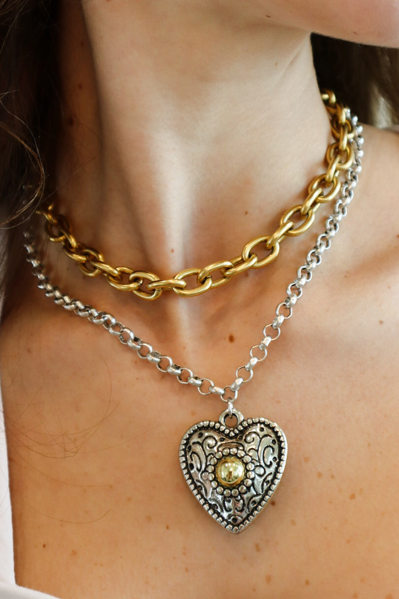 Vintage-inspired silver-tone heart pendant necklace with intricate engravings, gold-tone center accent, and dual-layered silver and gold chains for a bold statement look.