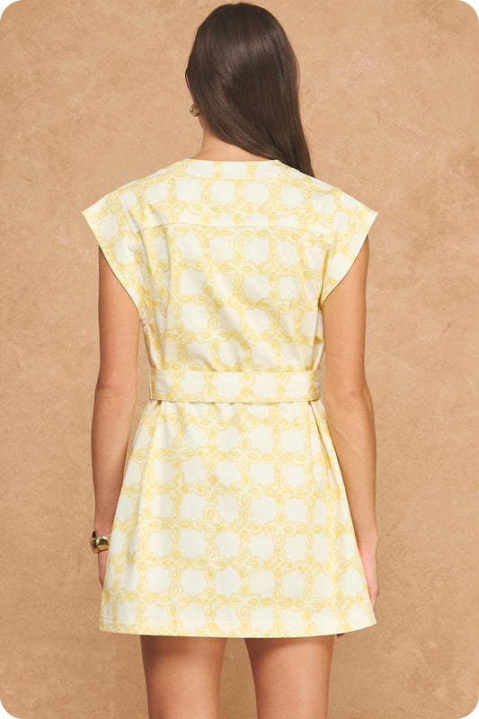 A sophisticated cotton twill mini dress featuring an exclusive chainlink print, structured sleeveless silhouette, metallic button details, and a statement belted waist.