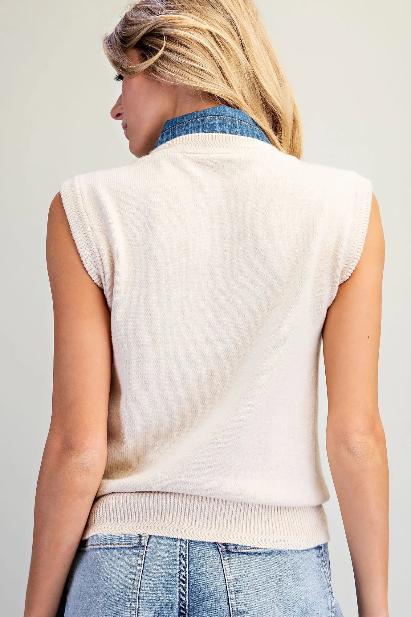 A stylish sleeveless knit top featuring a V-neckline, oversized denim tie-neck bow, and textured ribbed trim for a unique, polished look.