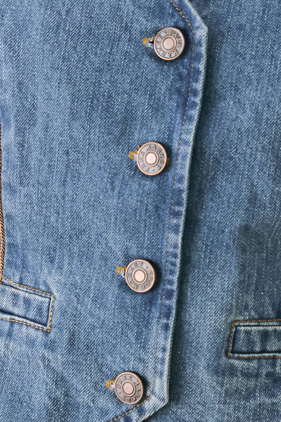 Close-up of a blue denim garment with four metallic bullet-shaped buttons aligned vertically along the front.
