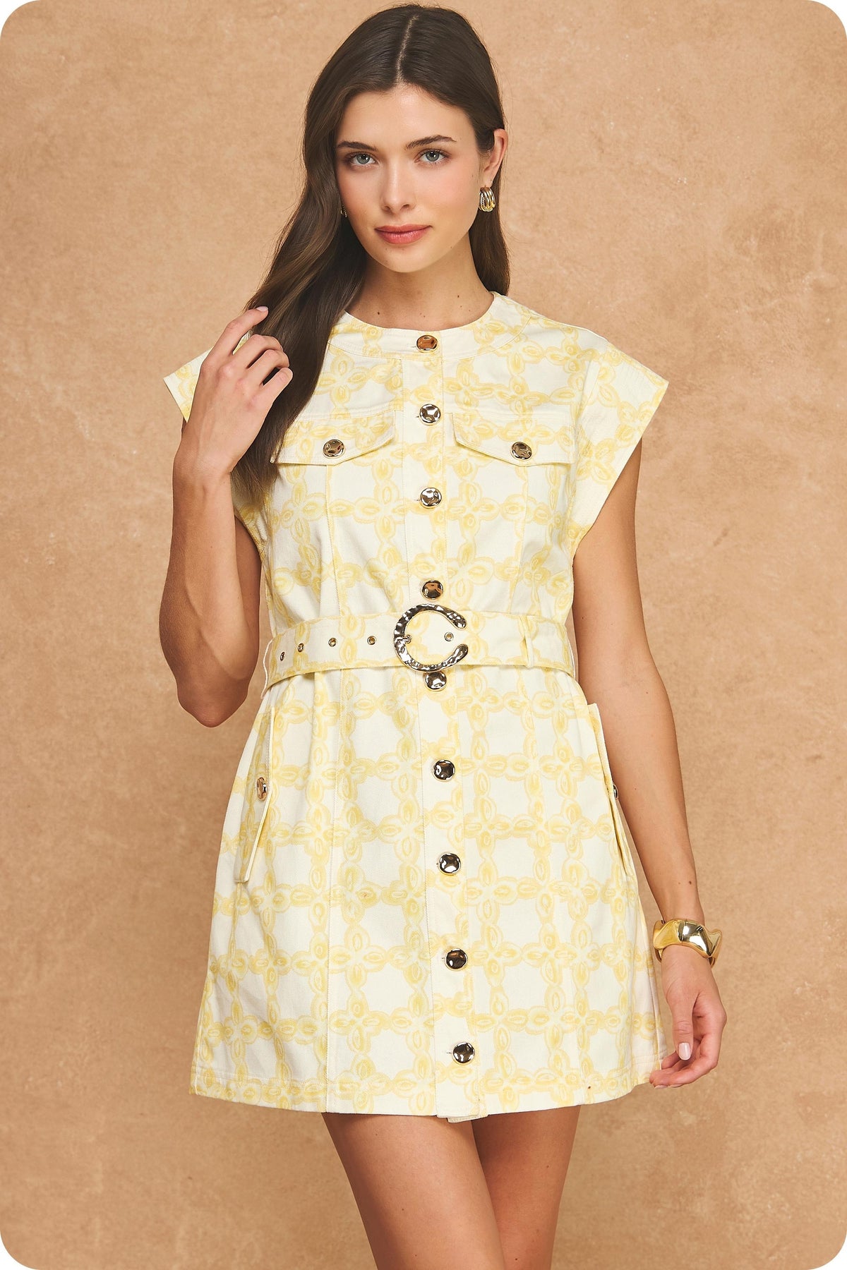 A sophisticated cotton twill mini dress featuring an exclusive chainlink print, structured sleeveless silhouette, metallic button details, and a statement belted waist.
