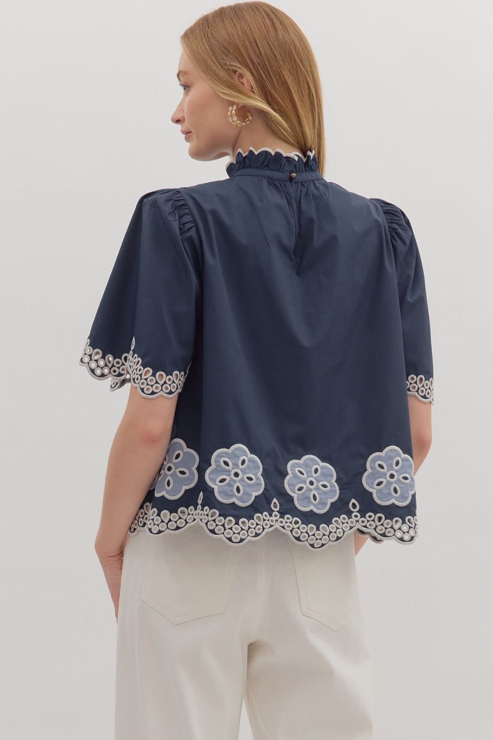 Romantic and airy, the Felicity top features floral embroidery, flutter sleeves, and a scalloped hem with a ruffled high neck.