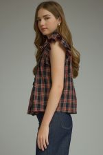 The Della Plaid Ruffle Sleeve Top combines classic plaid with feminine ruffle trim, a button-front placket, and polished collar detail.