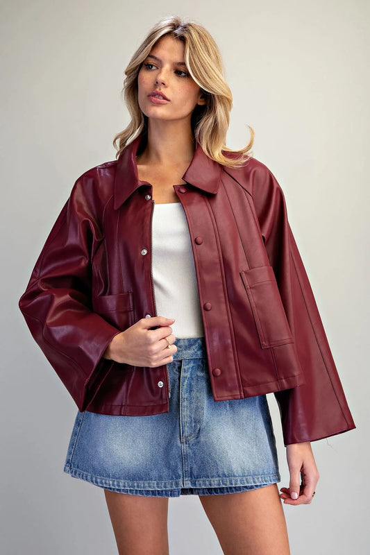 A fashion-forward pleather jacket featuring a flared boxy silhouette, dramatic wide raglan sleeves, paneled seams, and a sleek hidden zip-and-snap front.