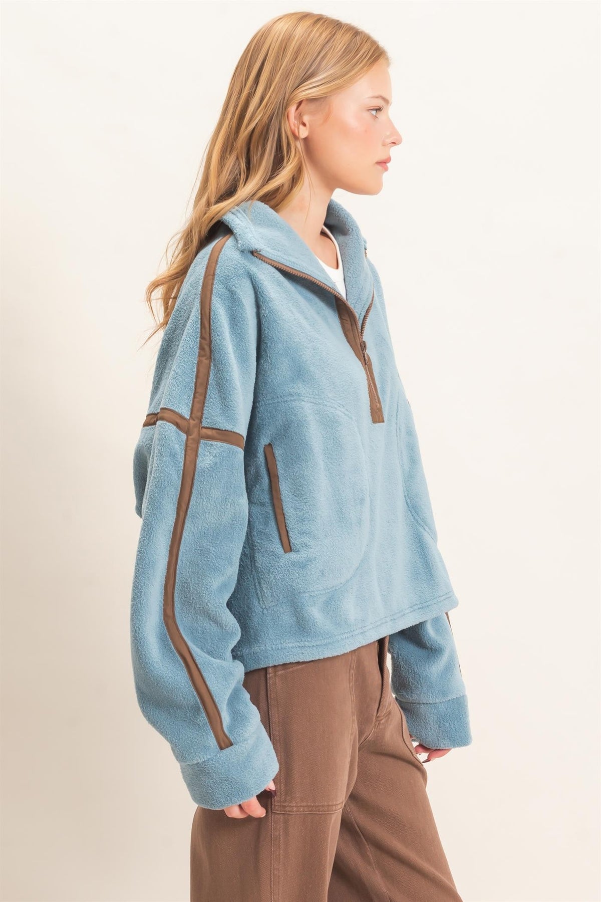 A cozy fleece half zip pullover featuring a high funnel neck, sporty contrast trim, oversized curved pockets, and an adjustable drawstring hem.