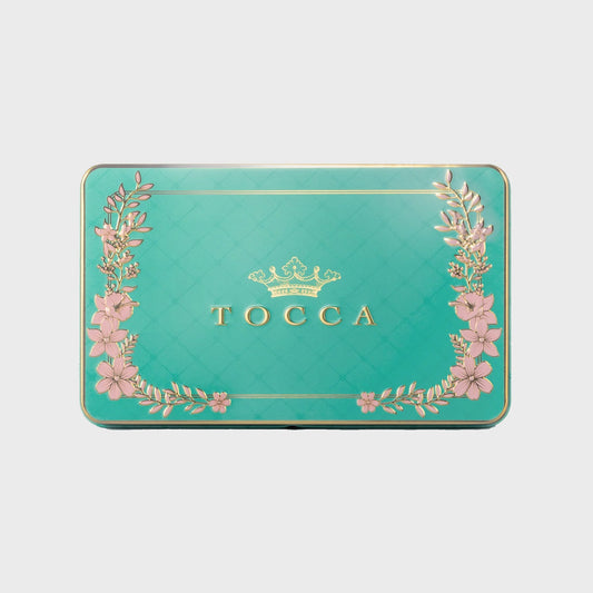 TOCCA product packaging with floral designs on a teal background