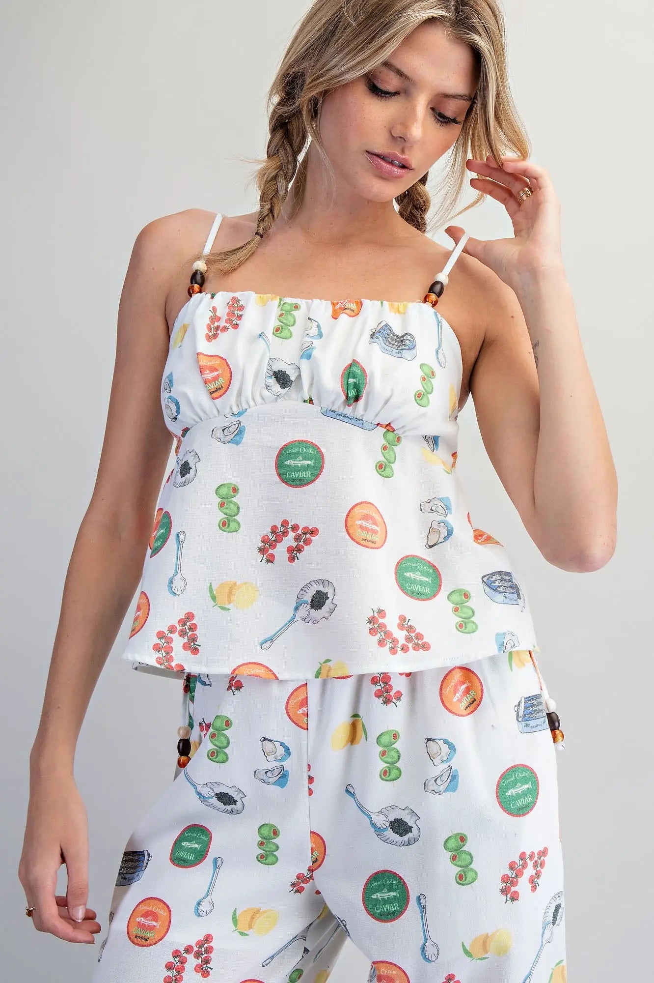 White Mediterranean-inspired food print babydoll top with adjustable beaded straps, gathered bust, and smocked back detail.