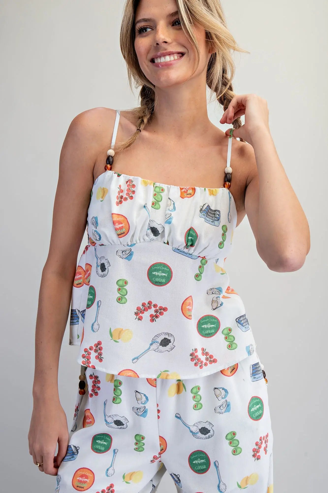 White Mediterranean-inspired food print babydoll top with adjustable beaded straps, gathered bust, and smocked back detail.