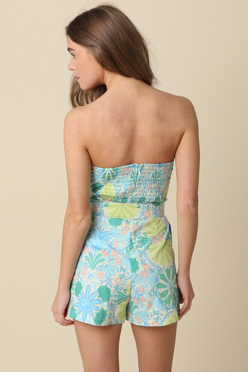 Woman wearing a strapless floral romper against a beige background