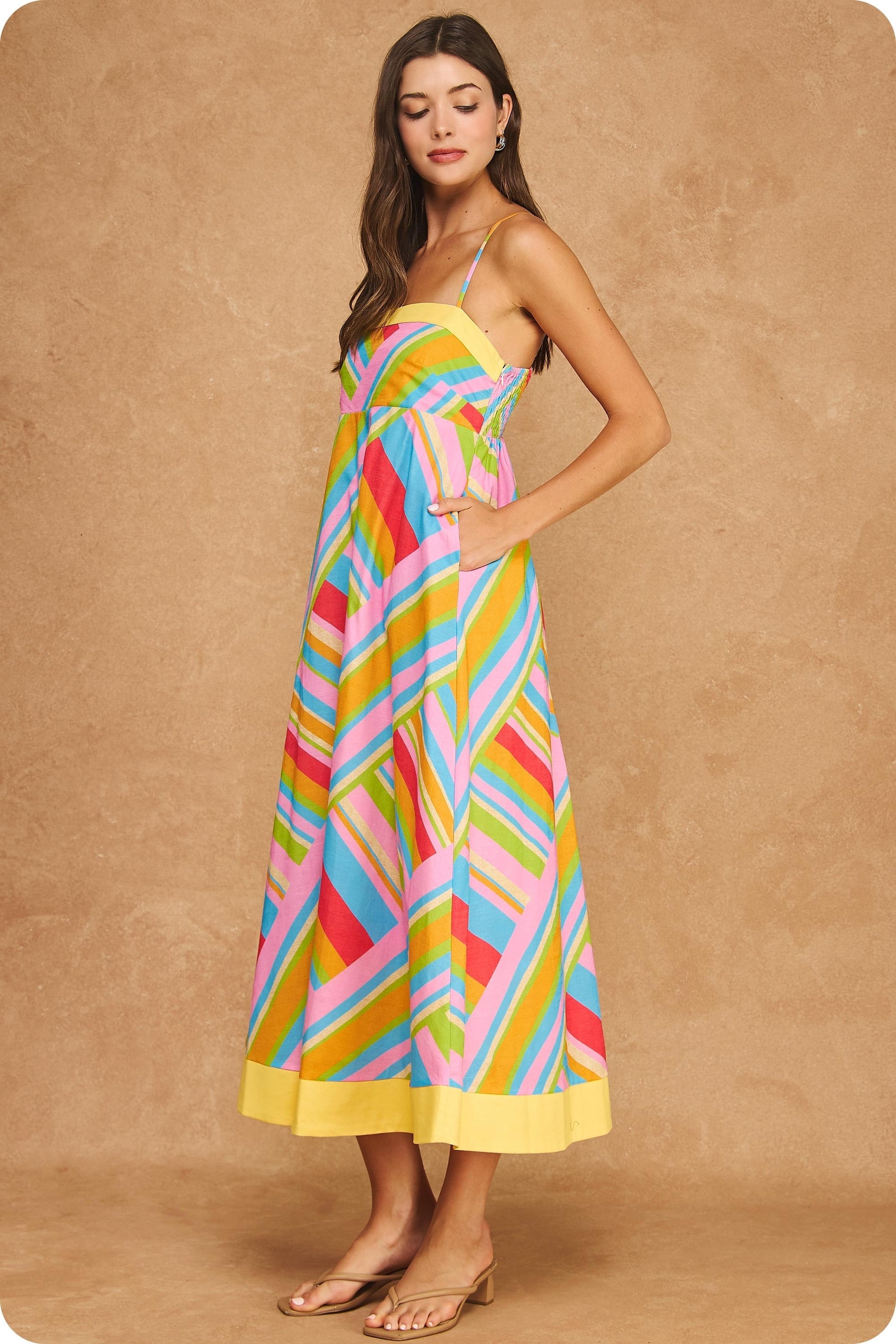 Colorful geometric stripe midi dress featuring a square neckline, adjustable spaghetti straps, empire waist silhouette, smocked back, hidden pockets, and contrast yellow trim.
