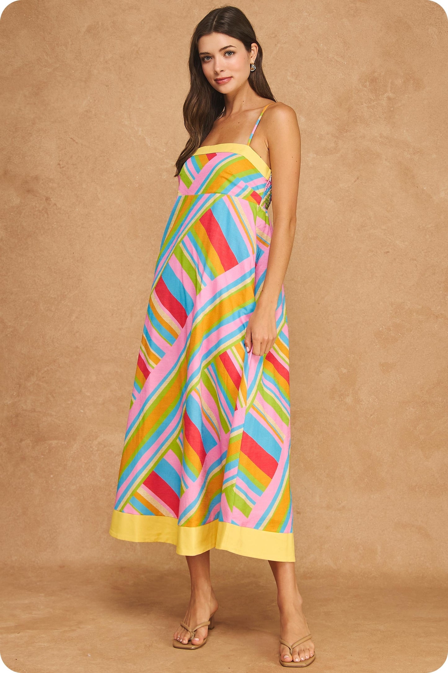 Colorful geometric stripe midi dress featuring a square neckline, adjustable spaghetti straps, empire waist silhouette, smocked back, hidden pockets, and contrast yellow trim.
