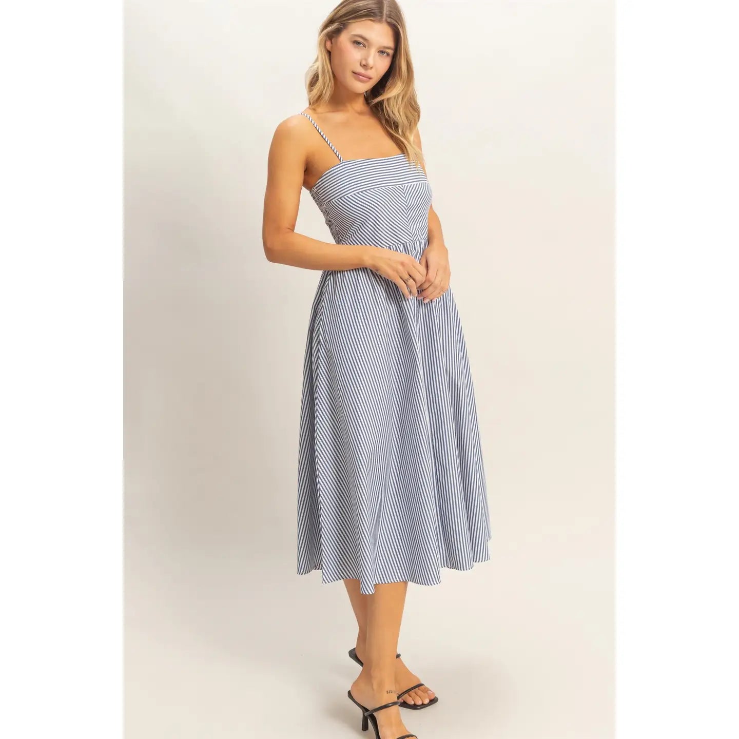 Woman wearing a blue and white striped midi sundress with spaghetti straps and fit-and-flare silhouette, lightweight summer dress styled with black sandals.