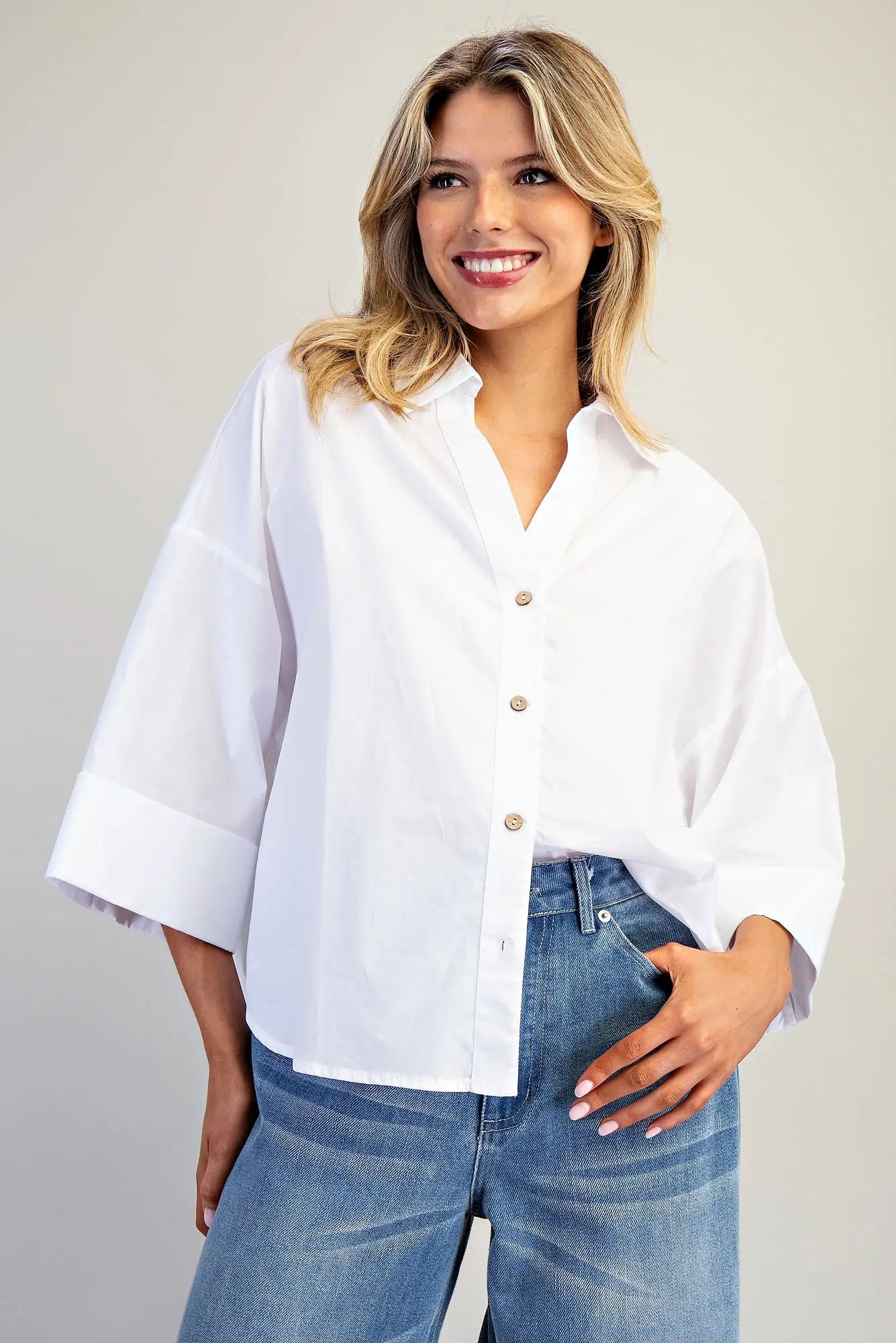 Woman wearing a white blouse and blue jeans against a plain background