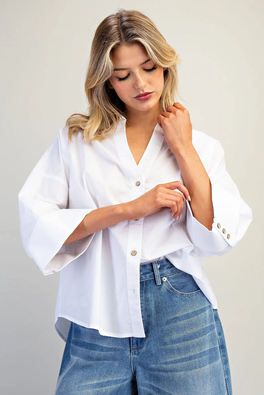 Woman wearing a white blouse with bell sleeves and blue jeans on a plain background