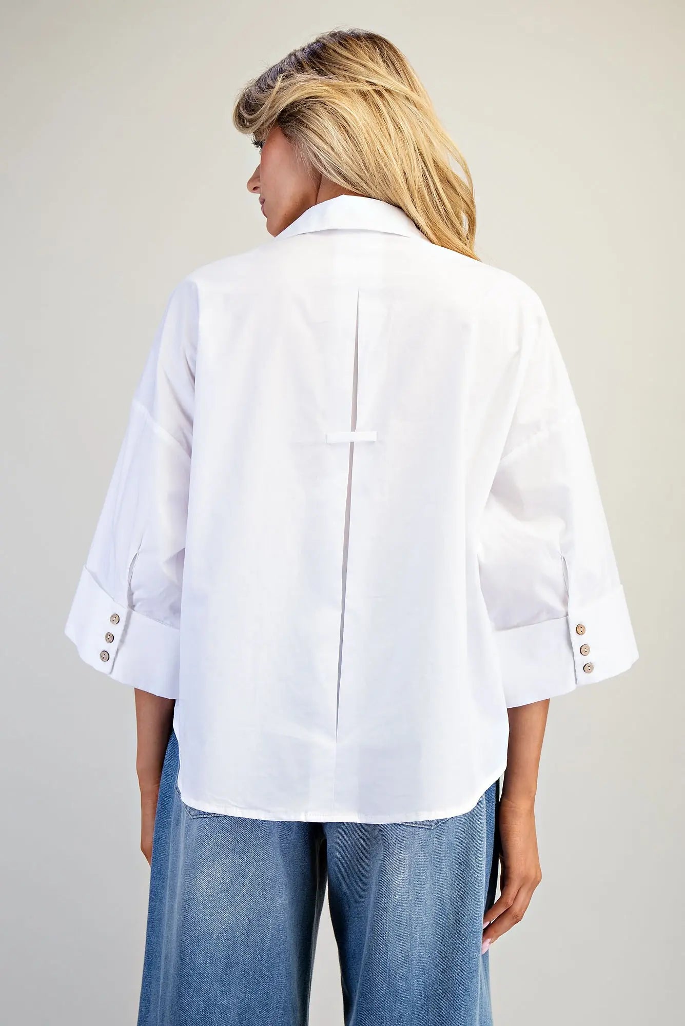 Person wearing a white blouse with rolled-up sleeves and blue jeans on a plain background