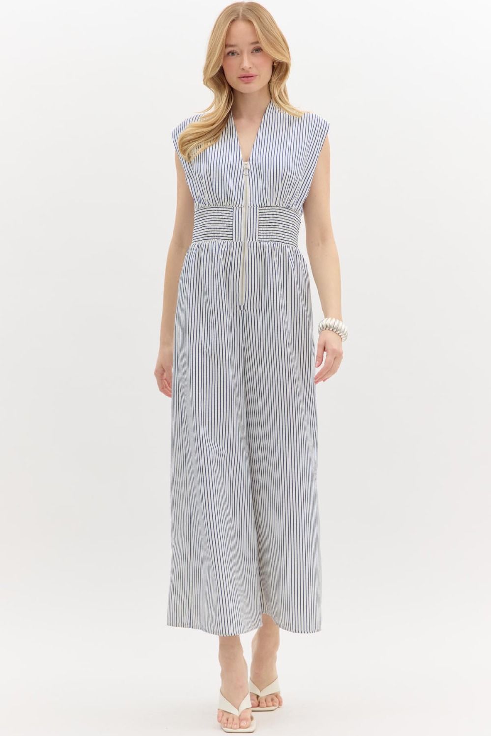 A sleek ankle-length jumpsuit with structured shoulders, front zipper, and smocked waist—tailored yet relaxed with coastal-cool appeal.