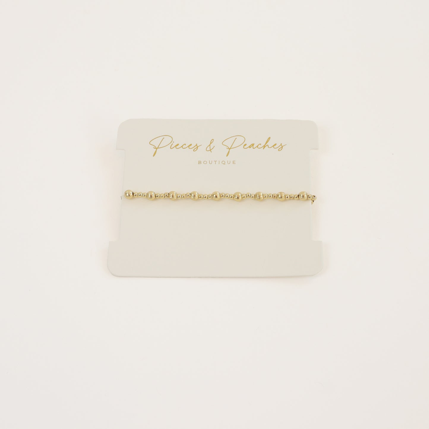 A delicate 14K gold-filled textured beaded bracelet displayed on a model's wrist, showcasing its elegant design and stackable style