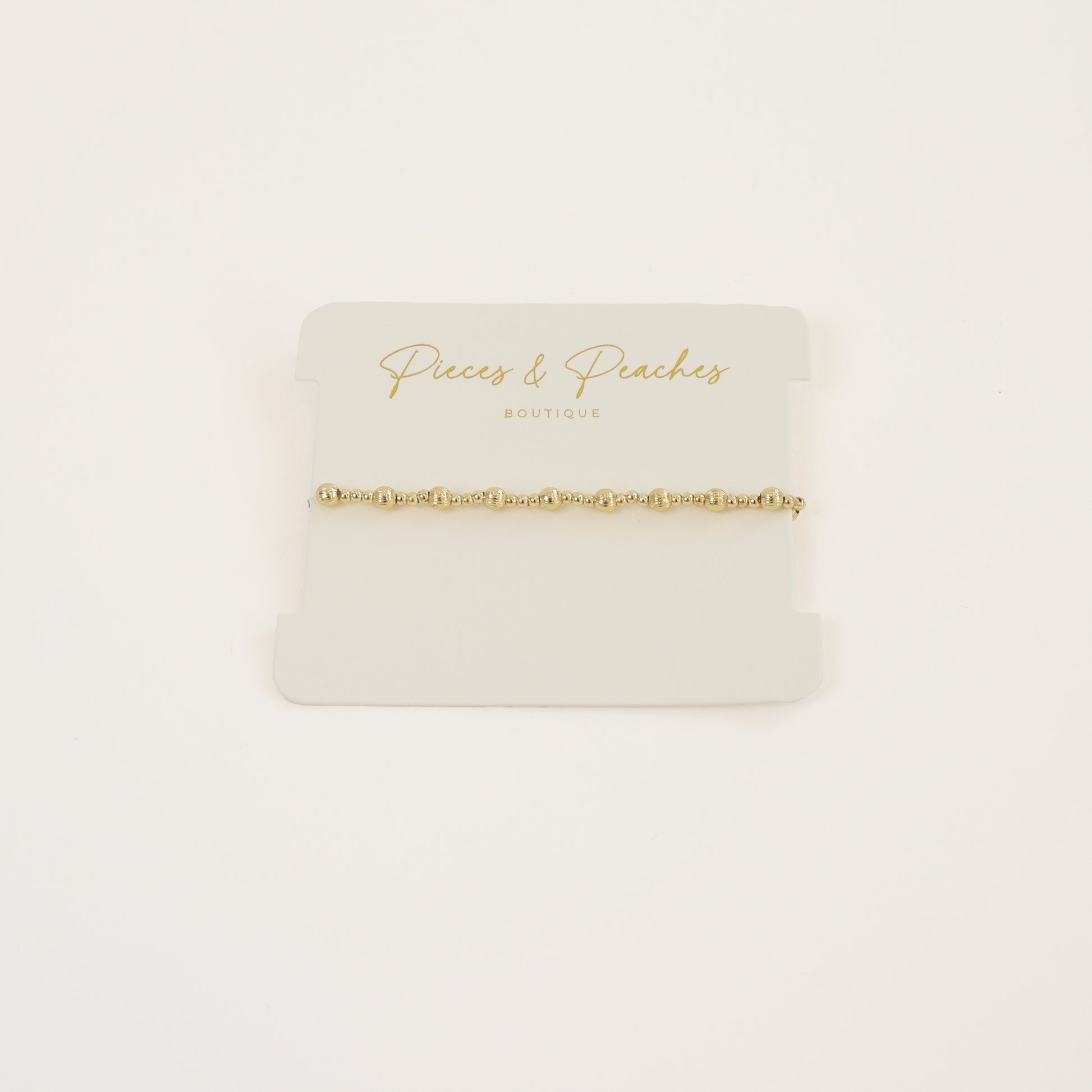 A delicate 14K gold-filled textured beaded bracelet displayed on a model's wrist, showcasing its elegant design and stackable style
