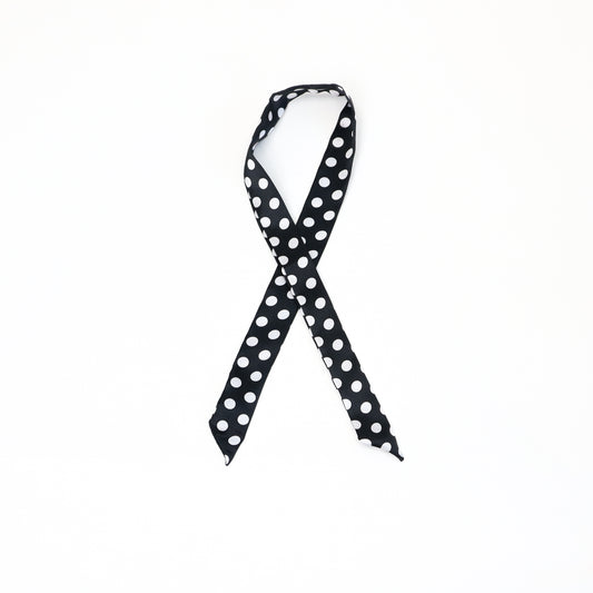 A slim twilly scarf with a classic black background and small white polka dots, tied in a loop.