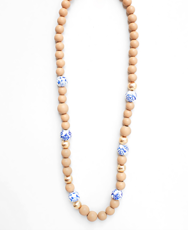 A long, beaded necklace featuring alternating natural light brown wooden beads and smaller gold-toned metallic spacer beads. Periodically, larger white beads with delicate blue floral patterns, reminiscent of porcelain or ceramic, are interspersed throughout the strand.