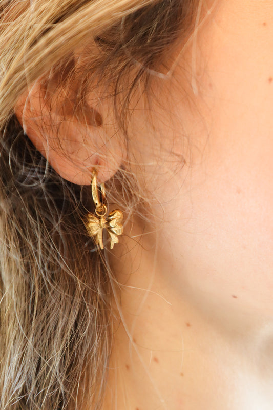 Gold huggie hoop earrings with delicate bow-shaped charms
