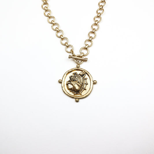 A bold gold-toned medallion necklace featuring an intricately detailed bulldog pendant on a chunky chain with a toggle clasp.
