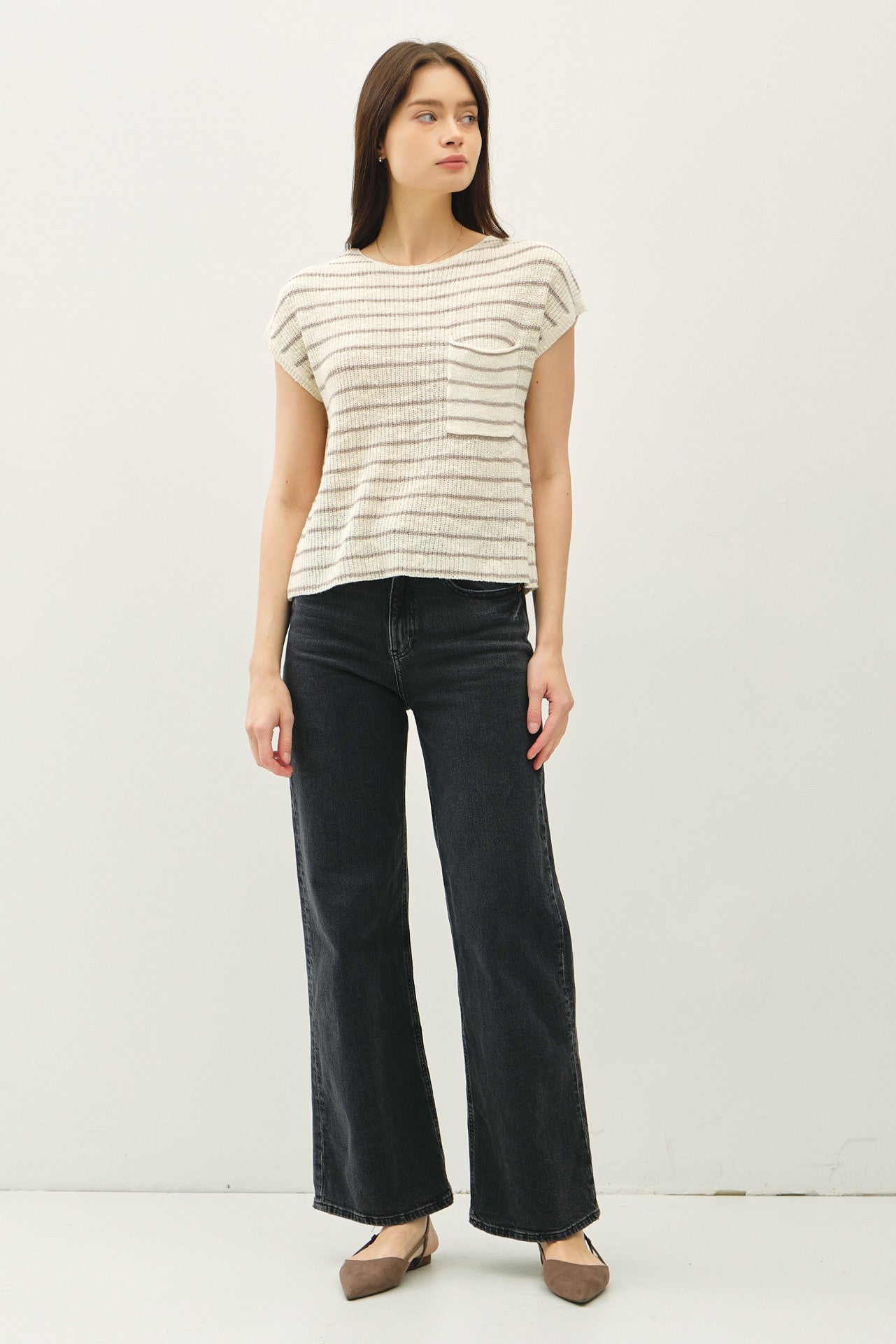 Women's beige and brown striped knit top with cap sleeves, a front pocket detail, and a relaxed fit, paired with black wide-leg jeans for a modern casual look.